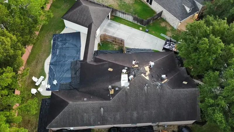 Roofing crew at work on a dark shingle roof, with a tarp protecting the back patio below