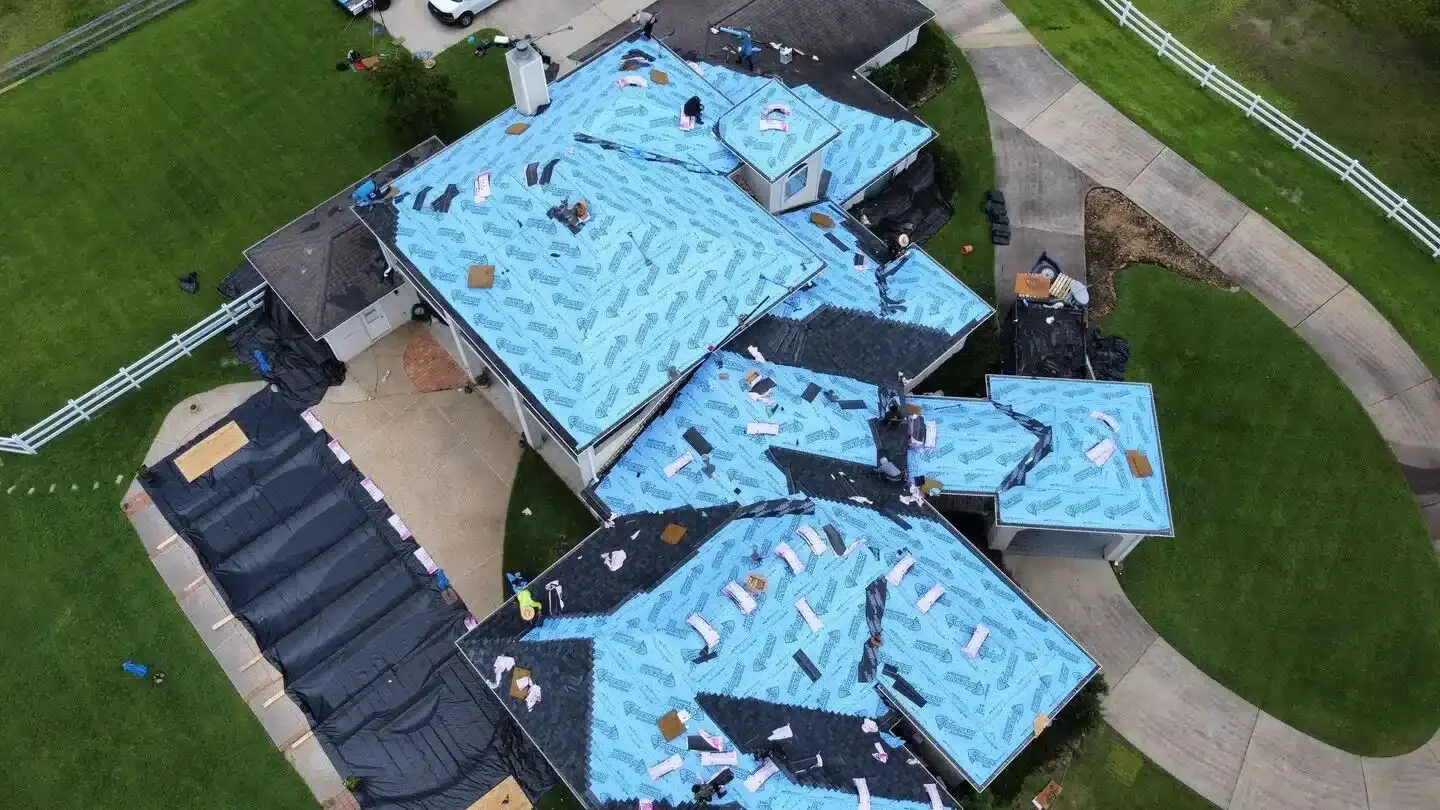 Home in the middle of a roof replacement, with the old shingles stripped and blue synthetic underlayment laid over the whole roof