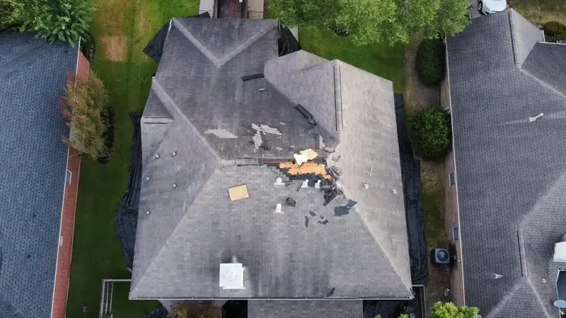 Aerial view of a gray shingle roof with a patch of shingles torn off, exposing the wood decking underneath